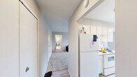 Located at 27435 Greenfield Rd in Southfield, Michigan, this one-bedroom, two-bathroom unit offers a thoughtfully laid-out single-floor plan with a clean, neutral aesthetic throughout. The living room is generously sized, featuring plush carpeting, large windows dressed with vertical blinds that allow abundant natural light, and a visible HVAC vent for year-round comfort. The kitchen is efficiently designed with light hardwood-style flooring, white cabinetry extending to the ceiling, white appliances including a range and refrigerator, and ample counter space — complemented by a pantry closet for extra storage. The bedroom is a comfortable retreat, benefiting from dual windows that brighten the room with natural light, soft carpeting, and a large closet. A second room off the hallway provides additional flexible space, also carpeted and well-lit. Two full bathrooms serve the unit; one features a wide vanity with dual sinks, white tile flooring, and direct hallway access, while the second includes a tub-shower combination with white tile surround. A connecting hallway ties all rooms together, creating a cohesive and functional flow throughout the unit.