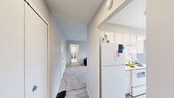 Located at 27435 Greenfield Rd in Southfield, Michigan, this one-bedroom, two-bathroom unit offers a thoughtfully laid-out single-floor plan with a clean, neutral aesthetic throughout. The living room is generously sized, featuring plush carpeting, large windows dressed with vertical blinds that allow abundant natural light, and a visible HVAC vent for year-round comfort. The kitchen is efficiently designed with light hardwood-style flooring, white cabinetry extending to the ceiling, white appliances including a range and refrigerator, and ample counter space — complemented by a pantry closet for extra storage. The bedroom is a comfortable retreat, benefiting from dual windows that brighten the room with natural light, soft carpeting, and a large closet. A second room off the hallway provides additional flexible space, also carpeted and well-lit. Two full bathrooms serve the unit; one features a wide vanity with dual sinks, white tile flooring, and direct hallway access, while the second includes a tub-shower combination with white tile surround. A connecting hallway ties all rooms together, creating a cohesive and functional flow throughout the unit.
