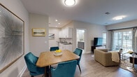 Located at 77 Gardnertown Rd in Newburgh, NY, this single-floor unit offers a thoughtfully designed open-concept layout that seamlessly connects the main living areas. Light wood-style flooring runs throughout, providing a cohesive and contemporary feel across every room.

The kitchen is well-appointed with white shaker cabinetry, gray countertops, a subway tile backsplash, and a full suite of stainless steel appliances, including a French door refrigerator, electric range, and built-in microwave. It flows directly into the dining area, which comfortably accommodates a four-seat table, and opens further into the living room—a generously proportioned space with room for ample seating and an in-unit stacked washer and dryer tucked nearby.

Two bedrooms are each finished with neutral-toned walls, hardwood-style flooring, and windows dressed with blinds and curtain panels that allow for adjustable natural light. The primary bathroom is notably spacious, featuring a dual-sink vanity with gray cabinetry, white countertops, large-format tile flooring, and a glass-enclosed walk-in shower with subway tile surround and a built-in bench. Clean lines, recessed lighting, and a neutral palette give the entire unit a polished, modern ambiance.