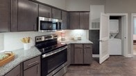 This single-floor residence offers a thoughtfully designed layout with modern finishes and a cohesive, neutral color palette that creates a warm and inviting atmosphere throughout. The kitchen is a standout feature, outfitted with dark espresso cabinetry, granite countertops, a classic subway tile backsplash, and a full suite of stainless steel appliances, including a range, microwave, and refrigerator. Rich wood-look flooring runs through the kitchen and main living areas, adding warmth and durability.

The living room is bright and welcoming, with large windows dressed in white curtains that invite generous natural light. Crown molding and a ceiling fan add refined detail to the space. The open flow between the living and kitchen areas makes the layout practical and social.

The bedrooms are carpeted for comfort, each offering ample space with ceiling fans or overhead lighting and access to closets. The primary bedroom connects to a well-appointed bathroom featuring granite countertops, dark cabinetry, wood-look flooring, and a full soaking tub with shower. A second full bathroom mirrors the same quality finishes. A walk-in closet is accessible from one of the bathrooms, providing excellent storage. Overall, the residence balances modern style with everyday functionality.