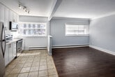 Located at 233 Mohawk Rd E in Hamilton, Ontario, this one-bedroom, one-bathroom unit offers a compact and efficiently designed layout across a single floor. The kitchen is a standout feature, showcasing tall white shaker-style cabinetry, stainless steel appliances including a full-size refrigerator, electric range, and over-the-range microwave, complemented by white subway tile backsplash and light ceramic tile flooring. A window above the counter invites natural light into the space. The living area transitions seamlessly from the kitchen and features light wood-style laminate flooring, soft grey walls, and a wall-mounted ductless air conditioning unit for year-round comfort. Baseboard heating is present throughout. The bedroom is a well-proportioned room with grey wood-tone laminate flooring, light grey walls, clean white baseboards and crown moulding, and a wall-mounted A/C unit. The bathroom is thoughtfully finished with white subway tile surrounding a full bathtub, accented by a decorative mosaic tile border, paired with a mirrored medicine cabinet. The unit maintains a consistent neutral colour palette of soft greys and whites, creating a clean, modern, and move-in-ready atmosphere throughout.