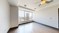 Located in the heart of Dallas at 1400 Pacific Ave, this modern 2-bedroom, 3-bathroom residence offers a well-designed single-floor layout with refined finishes throughout. The open-concept kitchen and living area is anchored by warm hardwood flooring, tray ceilings with crown molding, and ceiling fans that enhance the airy ambiance. The kitchen is outfitted with full stainless steel appliances — including a French door refrigerator, range, microwave, and dishwasher — complemented by sleek gray cabinetry, white quartz countertops, and a textured tile backsplash. The spacious primary bedroom features plush carpeting, a ceiling fan, and direct access to a generous walk-in closet with multi-tiered shelving. The second bedroom is a standout, boasting floor-to-ceiling windows that frame sweeping views of the Dallas skyline. Three well-appointed bathrooms include clean tile flooring, modern vanities with blue cabinetry accents, tiled shower enclosures, and built-in overhead storage. Two closets provide ample storage, and a dedicated laundry room with shelving adds practical convenience. Throughout, dark baseboards and dark-trimmed doors create a contemporary contrast against the neutral, light-toned walls, giving the space a polished, urban feel.