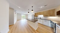 Located at 4101 Taylor Pond Ln in Billerica, MA, this thoughtfully designed one-bedroom, one-bathroom unit offers a clean, modern aesthetic throughout its well-appointed single floor. The open-concept kitchen and living area serves as the heart of the home, featuring light hardwood flooring that flows seamlessly across the space. The kitchen is outfitted with a two-tone cabinetry scheme — warm wood upper cabinets paired with crisp white lower cabinets — complemented by dark countertops, a subway tile backsplash, and a full suite of stainless steel appliances including a refrigerator, range, microwave, and dishwasher. A center island with pendant lighting adds additional prep and gathering space. The living area benefits from a large sliding glass door that invites abundant natural light and provides outdoor views. The spacious bedroom features large windows, light hardwood floors, a wall-mounted mini-split HVAC unit for individual climate control, and a stylish three-panel gray door. The bathroom is finished with large-format floor tile, a wood-accented vanity with white countertop, and a walk-in tiled shower with built-in shelving and a bench. A connecting hallway completes this well-designed, move-in-ready home.