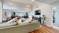 Located at 12355 Alcosta Blvd in San Ramon, CA, this single-floor open-concept space seamlessly integrates a living room, dining room, and kitchen into a cohesive and functional layout. Light hardwood flooring runs throughout, complementing the neutral, warm-toned walls and creating a clean, welcoming atmosphere.

The living area is anchored by a dramatic vaulted ceiling with a striking floor-to-ceiling window that floods the space with natural light. A large sectional sofa, wall-mounted television, and decorative cabinetry make this a comfortable and versatile gathering area.

The expansive dining room features a long, polished conference-style table with ample seating, ideal for group gatherings. Multiple windows and sliding glass doors provide direct views and access to an outdoor patio and pool area, enhancing the sense of openness and connectivity to the exterior.

The kitchen is efficiently designed with white cabinetry, light quartz countertops, and stainless steel appliances including a refrigerator, electric range, and microwave. A window above the counter brings in additional natural light, keeping the space bright and airy.

Overall, this well-appointed space offers a bright, modern, and communal environment well-suited for shared use and social gatherings.