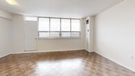 This 2-bedroom, 1-bathroom unit at 125 Neptune Drive in Toronto offers a well-organized layout across a single floor. The spacious living room is a standout feature, characterized by large multi-pane windows that flood the space with natural light and frame views of the surrounding neighbourhood. Warm parquet flooring runs throughout the living areas and bedrooms, adding a classic character to the interior.

The galley-style kitchen is efficiently designed with ample white cabinetry lining both walls, a tiled backsplash, beige countertops, a double sink, and white appliances including a stove and refrigerator. Light tile flooring completes the clean, functional aesthetic. A dedicated closet area off the kitchen provides additional storage and houses a stacked washer and dryer unit.

The primary bedroom is generously sized and benefits from a large window offering outdoor views, with parquet flooring continuing throughout. A second bedroom also features parquet floors and a built-in closet with folding doors. The full bathroom is finished with white wall tiles, a bathtub with overhead shower, and tile flooring. A hallway connects the rooms, completing the practical and cohesive floor plan.