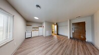 Located at 2215 E 56th St in Indianapolis, Indiana, this efficient one-bedroom, one-bathroom unit is thoughtfully laid out across a single floor. The interior is finished with light-toned wood-look luxury vinyl plank flooring throughout, complementing the neutral gray walls and white ceilings to create a clean, cohesive aesthetic.

The open main living area flows directly into the kitchen, which is equipped with a white electric range, a full-size refrigerator, a compact sink with under-counter cabinetry, and open wood shelving above. A window along the exterior wall allows natural light to filter into the space, providing views of the surrounding neighborhood.

The bedroom area is generously sized relative to the overall footprint and includes an open closet with a hanging rod for storage. A mirrored door adds a functional touch, while an additional shelving unit provides further organizational options. The solid wood entry door leads directly into this living zone.

The bathroom is finished in crisp white tones, featuring a full-size soaking tub with an integrated shower and built-in niche shelving, a toilet, and a sink. The clean, minimal design ensures ease of maintenance.

Overall, this unit offers a practical and efficiently designed living space with updated finishes, ample natural light, and essential amenities, well-suited for those seeking a straightforward and functional home in Indianapolis.