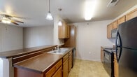 This single-floor residence offers a functional and cohesive layout connecting the main living areas through a well-designed open floor plan. The kitchen is a central feature, equipped with black appliances including a range, dishwasher, refrigerator, and over-the-range microwave. Warm medium-toned wood cabinetry provides ample storage, while dark laminate countertops extend along the workspace. A peninsula with a built-in breakfast bar separates the kitchen from the living area, accented by dual pendant lights that add a focused, practical glow. Tile flooring runs throughout the kitchen and hallway areas, offering durability in high-traffic zones.

The living room is generously sized, featuring plush carpeting, a ceiling fan with integrated lighting, and French doors that allow natural light and outdoor views. The bedrooms are carpeted and each include ceiling fans, with windows providing natural light. One bedroom features French doors, adding a distinctive touch.

The bathrooms feature tile flooring, wood vanity cabinetry with dark countertops, large mirrors, overhead vanity lighting, and wall-mounted medicine cabinets, contributing to a clean and organized aesthetic throughout the home.