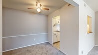 This single-story space features a straightforward, functional layout visible in the 3D floor plan, with rooms arranged for practical everyday living. The main living area is generously proportioned, finished with wall-to-wall carpet in a neutral gray tone and painted in warm beige. A ceiling fan with an integrated light fixture is centrally mounted, and a horizontal chair rail detail adds subtle architectural interest to the walls. A window allows natural light to filter into the space.

An adjacent bedroom offers comparable carpeted flooring, bright white walls, and two windows fitted with horizontal blinds, providing ample natural light and outdoor views. A closet and entry door are conveniently positioned within the room.

The compact kitchen is accessed through an open doorway and features white cabinetry, light countertops, a double-basin stainless steel sink with a chrome faucet, and a range. The hard-surface flooring provides easy maintenance in this area.

The bathroom includes tile flooring, a white vanity with storage below, and a full bathtub and shower combination with a curved surround. Throughout, the space maintains a clean, neutral palette with textured ceilings, creating a cohesive and functional environment.