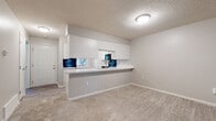 Located at 255 Lake Forest Blvd in Kalamazoo, Michigan, this single-floor residence offers a well-organized and functional layout with a clean, updated aesthetic throughout. The living room serves as a comfortable central gathering space, highlighted by a classic white-mantled fireplace and neutral carpet flooring, with a window allowing natural light to filter in. A staircase with a white baluster railing leads down to the main level, offering an open sightline toward the kitchen area. The kitchen is equipped with white cabinetry featuring brushed nickel hardware, light stone countertops, and black appliances including an electric range and over-the-range microwave. A pass-through peninsula connects the kitchen to the adjacent carpeted living and dining area, enhancing the open feel of the space. The bedrooms are generously sized, each featuring plush carpet flooring and windows that frame views of the surrounding greenery, filling the rooms with natural light. The bathroom showcases light wood-look flooring, white cabinetry with brushed nickel hardware, a white countertop vanity, and a well-lit hallway leading to additional rooms. Textured ceilings are present throughout, adding a consistent architectural detail across the home.