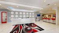 Located at 1410 Nottingham St in Huntsville, Texas, this single-story community clubhouse delivers a bold, contemporary design throughout its well-appointed spaces. The main lobby makes an immediate impression with its sparkling white reception desk, geometric circle wall décor on gray accent walls, large-format white tile flooring, and a striking red, black, and white area rug that sets the tone for the facility's vibrant aesthetic. A bar area with vivid red stools and shelved displays extends from the lobby, offering a social gathering point for residents.

The game room continues the high-energy design language with a bold red ceiling, three-dimensional geometric wall paneling, a pool table, ping pong table, plush white seating, and statement yellow pendant lighting — creating an energetic recreational retreat.

The fitness center is a standout amenity, divided into a cardio zone and a strength training area. The cardio section features rows of treadmills and ellipticals positioned before large windows with outdoor views, while the strength area is outfitted with a variety of resistance machines and free weights, complemented by floor-to-ceiling mirrors and polished dark concrete flooring.

The business center offers a refreshingly bright and creative workspace, featuring lime green carpeting, vibrant green ergonomic chairs, white Tulip-style tables, and modern pendant lighting — ideal for productivity. Accessible restrooms and ample natural light throughout complete this thoughtfully designed facility.