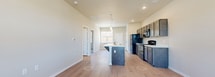 This single-story unit is designed with a functional, open-concept layout that connects the kitchen and living areas seamlessly. The kitchen serves as a central feature, equipped with dark-toned cabinetry, white countertops, and a full suite of black appliances including a refrigerator, gas range, built-in microwave, and dishwasher. A peninsula island with an integrated sink and breakfast bar overhang provides additional workspace and casual seating. Pendant lighting above the island and recessed ceiling lights contribute to a well-lit cooking environment. A window positioned above the sink allows natural light to fill the space.

Light wood-look flooring extends through the kitchen and main living area, complementing the neutral wall tones throughout. The living area is generously sized and includes a ceiling fan with a window that brings in additional natural light. A private entry door is accessible from this area. The bedrooms feature plush carpeting, ceiling fans, and windows with blinds that provide views to the exterior. The floor plan, visible in the 3D scan, reveals a well-organized layout with clearly defined living, kitchen, and bedroom zones, offering a practical and comfortable living environment.