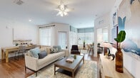 Located at 2150 NW 21st St in Ocala, Florida, this single-story residence offers a thoughtfully designed open-concept layout finished with warm hardwood-style flooring throughout. The inviting living area is bathed in natural light streaming through multiple large windows dressed with elegant blinds and valances, complemented by a ceiling fan overhead. The space flows seamlessly into a dedicated dining nook, creating an ideal setting for both relaxing and entertaining.

The kitchen is a standout feature, showcasing crisp white cabinetry, gleaming granite countertops, stainless steel appliances, and a generous island with bar seating and pendant lighting above. A separate galley-style workspace with additional granite counter surface provides practical functionality.

The bedrooms are comfortably sized with ample natural light and feature a serene, neutral aesthetic. The primary bathroom offers a dual-sink vanity topped with granite, large mirrors, and clean white cabinetry. A spacious walk-in closet with wire shelving provides generous storage.

The welcoming entryway hallway features tasteful wall art and console storage, setting the tone for the home's modern, well-curated interior. Clean white walls and consistent flooring throughout create a cohesive, light-filled ambiance across every room.
