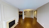 This single-floor residence showcases a thoughtfully designed open-concept layout that seamlessly connects the living, dining, and kitchen areas. Rich, dark hardwood flooring extends throughout the main living spaces, lending warmth and continuity to the interior. The living room is anchored by a classic fireplace framed with elegant wainscoting panel detailing, adding a refined architectural touch to the space. Neutral, warm-toned walls complement the dark wood tones and create a welcoming ambiance throughout. The dining area is defined by a stylish pendant light fixture that adds a focal point and soft illumination to the space. Adjacent to the dining area, the kitchen features dark cabinetry, stainless steel appliances, and a decorative tile backsplash, combining both functionality and style. A breakfast bar provides a convenient transition between the kitchen and dining spaces. A hallway leads further into the residence, offering access to additional rooms beyond the main living area. The textured ceiling and clean white baseboards and trim provide a polished finish throughout. Overall, the space offers a classic yet contemporary feel, ideal for both everyday living and entertaining.