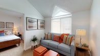 This single-floor residence offers a thoughtfully designed layout that maximizes both comfort and functionality. The living area is a standout space, featuring a dramatic vaulted ceiling with a textured finish that adds architectural character. A large window with horizontal blinds fills the room with natural light, while warm hardwood-style flooring transitions seamlessly to plush carpeting underfoot. The entryway opens directly into the living space, which provides generous room for seating and relaxation.

The kitchen is efficiently arranged in an L-shaped configuration, complete with white cabinetry accented by wood trim, granite-look countertops, white appliances including a refrigerator, electric range, and dishwasher, and hardwood flooring that extends throughout the main living and dining areas.

The bedroom is a serene retreat, featuring soft carpeting, a bright window for natural light, and a walk-in closet offering ample storage. Textured ceilings continue throughout, maintaining a consistent design aesthetic.

The bathroom is well-equipped with a vanity featuring granite-look countertops, a large mirror, hardwood flooring, and a full tub and shower combination with tile surround. Overall, the space presents a warm, inviting ambiance with a cohesive neutral palette accented by rich, earthy tones.