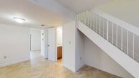 Located at 8324 NW Seventh St in Miami, FL, this two-story property offers a clean, functional layout spread across two well-defined levels. Throughout the space, warm-toned marble-style tile flooring provides a cohesive, polished look that carries through the main living areas, kitchen, and bathroom.

The main level features an open living area bathed in natural light from a large front-facing window dressed with vertical blinds. A solid entry door anchors the front of the space, while the layout flows efficiently toward the kitchen and a conveniently located bathroom. The kitchen is equipped with wood-toned cabinetry extending to the ceiling, granite-style countertops, and white appliances including a refrigerator, electric range, dishwasher, and range hood. The bathroom on this level includes a modern wood-finish vanity with a single sink, a large mirror with overhead lighting, and tiled walls.

A staircase with a metal railing connects the main level to the upper floor, which includes at least one bedroom featuring a closet with bi-fold doors and a window that brings in natural light. The overall interior presents a bright, neutral palette of white walls and light-toned finishes, creating a clean and versatile living environment.