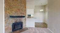 This single-story home at 3706 Block Dr in Irving, TX is defined by a dramatic floor-to-ceiling stone fireplace that anchors the living area, serving as a bold architectural focal point. The living space features neutral-toned carpet and transitions seamlessly into the dining area, which is illuminated by a classic chandelier pendant light and benefits from a large window and entry door that invite natural light throughout. A ceiling fan adds practical comfort to the living room.

The kitchen is designed in a galley layout, featuring white cabinetry on both sides, wood-look flooring, and black appliances including a range and microwave. A pass-through counter connects the kitchen to the living and dining spaces, enhancing the open flow of the layout.

The bedroom offers generous proportions, plush carpet, a window with natural light, and access to a walk-in closet with built-in shelving. The bathroom is appointed with a full-size soaking tub and shower combination with white tile surround, maintaining a clean and functional design throughout.

Overall, the home presents a cohesive, neutral palette with warm stone accents, creating a practical and comfortable living environment.