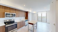 Located on the 13th floor at 218 NW Eighth St in Miami's vibrant urban core, this modern residence offers a thoughtfully designed open layout with clean lines and contemporary finishes throughout. The kitchen is a standout feature, showcasing warm walnut-toned cabinetry with sleek gold hardware, a crisp white subway tile backsplash, light quartz countertops, and a full suite of stainless steel appliances including a French door refrigerator, electric range, built-in microwave, and dishwasher. Large-format light tile flooring flows seamlessly from the kitchen into the open living area, enhancing the sense of spaciousness. Floor-to-ceiling windows and a sliding glass door lead to a balcony, flooding the interior with abundant natural light and framing expansive city and treetop views. The bedroom continues the bright, airy aesthetic with a ceiling fan and a tall window that captures sweeping Miami skyline views. The bathroom features elegant marble-look tile in the tub/shower surround, adding a refined, upscale touch. Recessed lighting throughout and crisp white walls contribute to the unit's clean, modern ambiance, making this a polished and well-appointed residence in the heart of Miami.