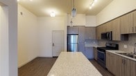 This thoughtfully designed 2-bedroom, 2-bathroom residence offers a modern living experience across a single floor. The open-concept kitchen serves as a centerpiece of the home, featuring stainless steel appliances including a French door refrigerator, gas range, and built-in microwave. Sleek, wood-toned cabinetry extends to the ceiling, maximizing storage and adding a refined aesthetic. A decorative tile backsplash adds texture and visual interest, while the expansive granite-topped island provides generous prep space and casual seating. Pendant lighting above the island and track lighting overhead create a layered, well-lit environment. Rich wood-look flooring flows throughout the main living areas, grounding the space with warmth and continuity. Soaring ceilings lend an airy, open feel to the living and kitchen areas, enhancing the sense of space. The neutral color palette throughout creates a clean, versatile backdrop ready for personalization. The front entry features a modern door with a keypad lock, combining convenience with security. Overall, this residence strikes a balance between contemporary style and everyday functionality, making it an inviting and practical place to call home.