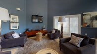 Located at 540 Carillon Pkwy in Saint Petersburg, Florida, this single-story community clubhouse offers an impressive range of amenities within a thoughtfully designed space. The entry makes an immediate statement with a soaring octagonal rotunda framed by stately white columns, a coffered ceiling painted in soft blue-gray, and light wood-look tile flooring laid in an elegant herringbone pattern. A decorative mosaic-topped center table anchors the space and sets the tone for the refined aesthetic throughout.

From the rotunda, wide corridors with rich navy-blue walls and tall ceilings lead to the various amenity areas. The lounge features comfortable seating, wall-mounted television, plantation shutters, and a striking arched window that draws in natural light. A coffee and refreshment bar adds to the relaxed, hospitality-inspired atmosphere.

The fitness center is well-equipped with multiple treadmills, elliptical machines, and strength equipment, all set beneath vaulted ceilings with large windows offering views of the outdoor greenery and full-wall mirrors that amplify the sense of space.

A dedicated business center provides dual workstations with monitors, floating wood-accented desks, and coordinating navy carpeting, offering a quiet and functional environment. Additional private rooms with seating and natural light round out the offering, making this clubhouse a versatile and welcoming hub for residents.