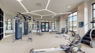 This contemporary fitness center is thoughtfully designed to support a full range of workout disciplines across a spacious, single-level layout. The space is immediately distinguished by its striking hexagonal LED lighting system, which traces geometric patterns across the ceiling and provides bright, even illumination throughout the main workout area. Neutral-toned carpet flooring and crisp white walls create a clean, modern aesthetic throughout.

The main training floor is generously outfitted with TRX functional training rigs, adjustable weight benches, a full dumbbell rack, and a punching bag, catering to both strength and functional fitness routines. Multiple Ski-Row machines, rowing ergometers, treadmills, elliptical trainers, and stationary bikes are arranged to maximize floor space and workflow. Large, black-framed floor-to-ceiling windows line the perimeter, flooding the space with natural light and offering open outdoor views.

A dedicated cycling studio features smooth hardwood-style flooring, a full wall of mirrors, and a row of professional spin bikes, separated from the main floor by sleek glass-panel partitions with navy-framed doors. An additional area houses a Body-Solid medicine ball and stability ball storage rack alongside supplementary cardio equipment. The combination of purposeful zoning, abundant natural light, and premium equipment makes this fitness center a comprehensive and inviting training facility.