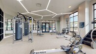 This contemporary fitness center is thoughtfully designed to support a full range of workout disciplines across a spacious, single-level layout. The space is immediately distinguished by its striking hexagonal LED lighting system, which traces geometric patterns across the ceiling and provides bright, even illumination throughout the main workout area. Neutral-toned carpet flooring and crisp white walls create a clean, modern aesthetic throughout.

The main training floor is generously outfitted with TRX functional training rigs, adjustable weight benches, a full dumbbell rack, and a punching bag, catering to both strength and functional fitness routines. Multiple Ski-Row machines, rowing ergometers, treadmills, elliptical trainers, and stationary bikes are arranged to maximize floor space and workflow. Large, black-framed floor-to-ceiling windows line the perimeter, flooding the space with natural light and offering open outdoor views.

A dedicated cycling studio features smooth hardwood-style flooring, a full wall of mirrors, and a row of professional spin bikes, separated from the main floor by sleek glass-panel partitions with navy-framed doors. An additional area houses a Body-Solid medicine ball and stability ball storage rack alongside supplementary cardio equipment. The combination of purposeful zoning, abundant natural light, and premium equipment makes this fitness center a comprehensive and inviting training facility.