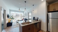 Located on N Lincoln Ave in Urbana, Illinois, this single-floor unit showcases a contemporary design with high-end finishes throughout. The open-concept living and kitchen area serves as the heart of the space, where striking herringbone-patterned hardwood flooring flows seamlessly underfoot. The kitchen is well-appointed with stainless steel appliances, including a refrigerator, range, microwave, and dishwasher, complemented by granite countertops, a subway tile backsplash, and a mix of warm wood and white upper cabinetry. A central island with an undermount sink and pendant cage lighting above creates a natural gathering point that opens directly to the living area.

The living space benefits from an abundance of natural light through large windows, with a ceiling fan overhead adding to the airy atmosphere. Bar seating along the island connects the kitchen and living areas effortlessly, while a separate room adjacent to the living space provides a dedicated workspace or study area.

Each bedroom features plush carpeting, a ceiling fan, large windows for natural light, and a built-in bed-and-desk unit with integrated shelving. Private bathrooms accompany each bedroom, finished with herringbone-tiled flooring, granite vanities, and warm wood cabinetry. Walk-in closets with built-in shelving and hanging systems are accessible directly from each bathroom, offering generous storage throughout.