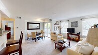 Located at 9801 Germantown Pike in Lafayette Hill, Pennsylvania, this well-appointed one-bedroom, one-bathroom residence offers a thoughtfully designed single-floor layout. The open-concept living and dining area forms the heart of the home, bathed in natural light from multiple windows and a sliding glass door that opens to a private balcony with outdoor views. The living space features plush carpeting, neutral tones, and a seamless flow between the sitting and dining areas, making it ideal for both relaxing and entertaining. The galley-style kitchen is efficiently organized with light wood cabinetry, ample counter space, a double sink, and tile flooring, providing everything needed for everyday cooking. The bedroom is a calm and comfortable retreat, offering generous proportions, soft carpeting, a large window with natural light, and direct access to a walk-in closet. The bathroom features light wood vanity cabinetry, a wide mirror with overhead lighting, and a clean, neutral palette that complements the rest of the home. Throughout the residence, a consistent use of soft whites and warm neutrals creates a bright and welcoming ambiance, making this an inviting and functional living space.