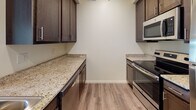 This single-floor residence offers a thoughtfully designed layout that balances comfort and functionality. The open living area is finished with warm wood-look laminate flooring and features a ceiling fan, creating a bright and airy atmosphere enhanced by natural light streaming through the windows. The galley-style kitchen is well-equipped with rich dark cabinetry, granite countertops, stainless steel appliances including an electric range and built-in microwave, and a dishwasher — providing ample workspace and storage. The bedrooms are carpeted for comfort and each benefit from natural light through blinds-fitted windows, with ceiling fans adding to the pleasant environment. Two bathrooms are finished in neutral tile, each featuring dark wood vanities with granite countertops. The primary bathroom includes a walk-in glass-door shower with tile surround and grab bar accents, while the second bathroom offers a similarly refined vanity setup. A dedicated laundry room houses a full-size top-load washer and dryer, adding everyday convenience. Throughout the space, a consistent warm neutral color palette and quality finishes create a cohesive and inviting atmosphere.