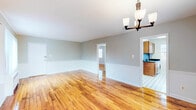 This single-floor residence offers a thoughtfully designed layout with a consistent, clean aesthetic throughout. The open living and dining area is a standout, featuring gleaming polished hardwood floors that extend throughout the main living spaces. Soft gray walls are accented by white chair rail molding, lending a classic, refined character to the room. A traditional multi-bulb chandelier serves as a focal point overhead, while a radiator and window unit provide climate control. Natural light filters in through multiple windows dressed with blinds, offering views of the surrounding neighborhood.

The kitchen is well-equipped with warm medium-toned wood cabinetry, dark granite countertops, and a striking mosaic tile backsplash. A stainless steel gas range anchors the cooking area, complemented by ample cabinet storage and a stainless sink. The classic black-and-white geometric tile flooring adds a timeless touch.

The bedrooms continue the hardwood flooring and feature ceiling fans, generous natural light from multiple windows, and built-in closets with shelving. The bathroom is finished with a sleek sliding glass-enclosed shower stall, a cast-iron radiator, and a bright window, creating a clean, functional space throughout.