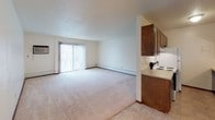 Located at 400 S Sneve Ave in Sioux Falls, South Dakota, this single-floor unit offers a practical and comfortable layout suited for everyday living. The open living area is generously sized, featuring plush wall-to-wall carpeting, a textured ceiling, and a ceiling fan with integrated lighting. A large sliding glass door floods the space with natural light and provides access to the outdoors, making the living area feel bright and airy. The kitchen is designed for efficiency, featuring rich dark wood cabinetry that lines both upper and lower sections, a double-basin sink, tile flooring, and white appliances including an electric range and refrigerator. A ceiling fan is also present in the kitchen area. Adjacent to the kitchen is an entry area with tile flooring, a front door with a sliding closet for storage, and a ceiling fan overhead. The bathroom is clean and functional, equipped with a full-size soaking tub and shower combination, tiled surround, chrome fixtures, and tile flooring. The layout of the unit flows smoothly between spaces, with transitions between carpeted and tiled areas clearly defined. Overall, the unit presents a straightforward, well-maintained living environment in a convenient Sioux Falls location.