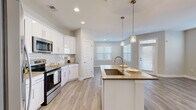 Located at 111 Grove Park Dr in Mooresville, NC, this well-appointed single-story home offers three bedrooms, two bathrooms, and a thoughtfully designed open-concept layout. The kitchen is a standout feature, showcasing crisp white cabinetry, a classic subway tile backsplash, quartz-tone countertops, stainless steel appliances including a side-by-side refrigerator and electric range, and a central island with a undermount sink and pendant lighting. Light wood-look LVP flooring runs throughout the main living areas, adding warmth and continuity. The living room benefits from multiple windows dressed with white blinds, allowing generous natural light to fill the space, and a glass-paneled entry door adds to the bright, airy feel. Well-lit hallways with recessed lighting connect the bedrooms and bathrooms seamlessly. The primary bedroom features plush carpet, multiple windows, and a walk-in closet outfitted with wire shelving systems for organized storage. Secondary bedrooms are also carpeted and include ceiling fans and natural light. The bathrooms feature white vanity cabinetry with neutral countertops and LVP flooring. Clean neutral tones and modern finishes throughout give the home a fresh, move-in-ready aesthetic.