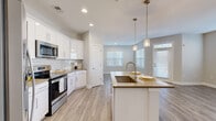 Located at 111 Grove Park Dr in Mooresville, NC, this well-appointed single-story home offers three bedrooms, two bathrooms, and a thoughtfully designed open-concept layout. The kitchen is a standout feature, showcasing crisp white cabinetry, a classic subway tile backsplash, quartz-tone countertops, stainless steel appliances including a side-by-side refrigerator and electric range, and a central island with a undermount sink and pendant lighting. Light wood-look LVP flooring runs throughout the main living areas, adding warmth and continuity. The living room benefits from multiple windows dressed with white blinds, allowing generous natural light to fill the space, and a glass-paneled entry door adds to the bright, airy feel. Well-lit hallways with recessed lighting connect the bedrooms and bathrooms seamlessly. The primary bedroom features plush carpet, multiple windows, and a walk-in closet outfitted with wire shelving systems for organized storage. Secondary bedrooms are also carpeted and include ceiling fans and natural light. The bathrooms feature white vanity cabinetry with neutral countertops and LVP flooring. Clean neutral tones and modern finishes throughout give the home a fresh, move-in-ready aesthetic.