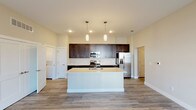 This single-story residence is designed with a clean, contemporary aesthetic and a functional open-concept layout. The kitchen serves as a focal point, showcasing rich dark espresso cabinetry that extends to the ceiling for ample storage, complemented by bright white quartz-style countertops and a full suite of stainless steel appliances, including a refrigerator with ice maker, electric range, and built-in microwave. A large central island with an integrated sink provides additional workspace and casual seating potential, while pendant lighting adds a refined touch overhead. Recessed lighting and wood-look plank flooring carry throughout the main living and dining areas, creating a cohesive, modern feel.

The open living area is generously sized, with neutral-toned walls and multiple doorways connecting to private spaces. The bedroom features plush carpeting, elevated ceilings, a window with outdoor views, and direct access to a walk-in closet with built-in shelving. The primary bathroom is outfitted with a dual-sink vanity featuring dark cabinetry, white countertops, a large mirror, and an adjoining walk-in closet. A secondary bathroom offers a single vanity with matching finishes. An in-unit stacked washer and dryer complete this well-appointed space.