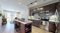 This single-floor residence offers a thoughtfully designed open-concept layout that seamlessly connects the kitchen, dining, and living areas. The kitchen is a standout feature, equipped with dark espresso cabinetry, stainless steel appliances including a range, microwave, dishwasher, and refrigerator, complemented by a light-toned tile backsplash and white countertops. A central island with built-in shelving and seating provides additional prep space and a casual dining option. Track lighting overhead enhances the kitchen's functionality and modern aesthetic.

Light wood-style flooring extends throughout the main living areas, creating a warm, cohesive feel. The living room is bright and airy, featuring a ceiling fan and large sliding glass doors that open to a private balcony with views of the surrounding exterior. Natural light flows generously into the space throughout the day.

The bedroom is carpeted for comfort, features a ceiling fan, and benefits from a large window that brings in ample natural light. The bathroom includes a dark-cabinetry vanity with a white countertop, a large mirror with vanity lighting, and clean large-format tile flooring, rounding out this well-finished residence.