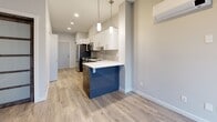 Located at 711 Treanor Avenue in Langford, BC, this efficiently designed unit offers a thoughtfully arranged single-floor layout that maximizes every square foot. The open-concept kitchen serves as the centerpiece of the space, outfitted with full stainless steel appliances including a French door refrigerator, electric range, over-the-range microwave, and dishwasher. Crisp white upper cabinetry contrasts with sleek dark lower cabinets, complemented by a light grey tile backsplash and white quartz countertops. A peninsula with a bold navy accent panel provides additional workspace and a casual dining area, illuminated by contemporary pendant lighting overhead. Light wood-tone laminate flooring flows throughout, enhancing the bright, airy feel of the unit. Recessed lighting and a wall-mounted mini-split system add to the modern functionality. The bathroom is clean and well-appointed, featuring a soaker tub with shower, vanity with storage, and tile flooring. In-suite laundry is conveniently accommodated with a stacked washer and dryer unit. Two closets provide practical storage solutions, and a private balcony offers an outdoor retreat with pleasant views of the surrounding greenery, bringing natural light into the living area.