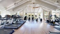 The Glenbrook Cardio Center in Cupertino, CA, is a thoughtfully designed fitness facility that combines an airy architectural aesthetic with a comprehensive array of cardio equipment. The space is defined by its striking vaulted ceiling with exposed white-painted beams, which lends a sense of openness and volume well beyond what the footprint alone might suggest. A large ceiling fan anchors the apex of the roofline, promoting air circulation throughout the workout area.

Natural light pours in generously through floor-to-ceiling windows that line multiple walls, offering unobstructed views of the surrounding mature trees and lush greenery — creating a refreshing, outdoor-connected atmosphere during every workout. The light-toned hardwood flooring adds warmth and is both practical and visually appealing.

The facility is stocked with a well-curated selection of cardio equipment, including multiple treadmills, elliptical trainers, stationary and cycling bikes, a rowing machine, and a stair climber. A full-length mirror along one wall amplifies the sense of space and allows users to monitor their form. A dumbbell rack and stability ball round out the strength and functional fitness options. The overall ambiance is bright, clean, and motivating — ideal for a focused cardiovascular workout.