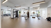 Located at 355 N Rosalind Ave in Orlando, FL, this modern fitness center spans a generously sized single floor, offering a well-organized and fully equipped workout environment. The space is divided into distinct functional zones, seamlessly connected to create a cohesive training experience.

The cardio area is lined with large floor-to-ceiling windows that flood the space with natural light and provide views of the outdoor surroundings, including a visible pool area. Treadmills, ellipticals, and stationary bikes are thoughtfully arranged to take advantage of these views. A dedicated functional training zone features a multi-use rig system with TRX suspension trainers, battle ropes, medicine balls, and a stall wall, catering to dynamic and bodyweight-based workouts.

The strength training section houses a full rack of dumbbells, cable machines, a power rack, adjustable benches, and a variety of selectorized machines. Durable rubber flooring throughout provides safety and comfort underfoot. Modern linear pendant lighting illuminates the entire facility, complementing the clean white walls and contemporary aesthetic.

A motivational mural anchors one end of the space, reinforcing an energizing atmosphere. A hydration station with dual water fountains is conveniently accessible near the entrance. The open floor plan and thoughtful equipment layout make this fitness center a comprehensive and functional facility.