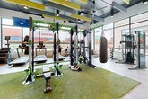Located at 397 N Central Ave in Hapeville, GA, this contemporary fitness center offers a well-appointed, single-floor exercise space designed for a comprehensive workout experience. The facility is thoughtfully divided into distinct training zones, seamlessly blending functionality with modern design.

The main workout area features artificial turf flooring that anchors a robust strength training zone, equipped with power racks, a heavy punching bag, battle ropes, dumbbells, and adjustable benches. Cardio equipment, including treadmills, lines the perimeter near floor-to-ceiling windows that flood the space with natural light and provide views of the surrounding area.

A separate section with polished concrete flooring houses a cable machine and barbell rack, complemented by large mirrors that enhance the sense of openness. The entry area welcomes users with a vibrant, colorful mural of a runner, setting an energetic tone, and includes a water fountain for added convenience.

Overhead, an exposed industrial ceiling with yellow acoustic panels, ceiling fans, and track lighting adds visual interest while maintaining comfort. The expansive window system throughout ensures the space feels bright and connected to the outdoors. The overall ambiance is energetic yet modern, making this fitness center a well-rounded facility suited for a wide range of training styles.