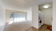 This single-floor residential unit offers a practical and comfortable layout designed for everyday living. The spacious living area is highlighted by large sliding glass doors fitted with vertical blinds, allowing abundant natural light to fill the room and providing views of the surrounding greenery. Plush wall-to-wall carpeting runs throughout the living and bedroom spaces, adding warmth underfoot, while durable wood-look flooring transitions into the kitchen and bathroom areas. A textured popcorn ceiling is consistent throughout the unit.

The galley-style kitchen is efficiently designed with white cabinetry offering generous storage, granite-toned countertops, and a full suite of white appliances including an electric coil range, refrigerator, and dishwasher. An overhead range hood and under-cabinet lighting enhance the functionality of the space.

The bedroom features a closet with a panel door, a baseboard heater, and a horizontal window that brings in soft, diffused natural light. The full bathroom is neatly appointed with a single vanity, granite-toned countertop, a mirrored medicine cabinet, and a shower/tub combination with a curtain enclosure. Baseboard heating is present throughout the unit, ensuring year-round comfort in this clean, move-in-ready space.