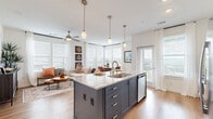 This thoughtfully designed 2-bedroom, 2-bathroom single-floor residence offers a comfortable and functional layout across a generous footprint. The open-concept living area seamlessly connects the kitchen, dining, and living spaces, all bathed in natural light streaming through large windows fitted with elegant plantation shutters and sheer curtains. The kitchen is a standout feature, showcasing a large center island with granite countertops, an integrated sink, pendant lighting, stainless steel appliances, and crisp white cabinetry — ideal for both cooking and entertaining. The dining area occupies a bright corner nook with floor-to-ceiling windows offering outdoor views. The living room is equally sun-drenched, with a ceiling fan and warm hardwood-style flooring that flows throughout the main areas. The primary bedroom is a comfortable retreat, complete with plush carpeting, a ceiling fan, and access to a well-appointed en-suite bathroom featuring a double granite vanity, glass-enclosed shower, and tile flooring. A spacious walk-in closet with wire shelving provides ample storage. A dedicated laundry room adds everyday convenience. The residence also includes a balcony, an entrance foyer, and a second full bathroom, rounding out a complete and practical living experience.