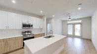 Located in McKinney, TX, this thoughtfully designed 2-bedroom, 1-bathroom residence offers a clean, contemporary aesthetic with a functional single-floor layout. Light wood-style flooring runs throughout, complementing the bright white walls and creating a warm, cohesive feel across all living areas.

The kitchen serves as the centerpiece of the home, featuring a large center island with an undermount sink, crisp white upper cabinetry, warm wood-toned lower cabinets, and a classic tile backsplash. Stainless steel appliances — including a French door refrigerator, range, and built-in microwave — complete this modern and well-equipped space. Recessed lighting overhead adds a polished finish.

The spacious primary bedroom offers generous proportions and connects directly to the full bathroom and a large walk-in closet. The bathroom is outfitted with a wood-toned vanity, subway tile tub-and-shower combination, and matching light flooring. A second walk-in closet with built-in shelving and hanging rods provides excellent storage.

The second bedroom features a ceiling fan, natural light from a window with outdoor views, and its own dedicated closet. Both bedrooms maintain the home's clean, neutral palette. Overall, the space delivers a bright, modern living environment with practical storage solutions and quality finishes throughout.