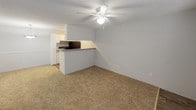 This single-floor residential unit offers a practical and comfortable layout designed for everyday living. The open living area is finished with warm beige carpeting and features a ceiling fan with integrated lighting, creating a bright and airy atmosphere. A peninsula-style kitchen counter separates the living space from the kitchen, providing a natural transition between the two areas.

The kitchen is well-appointed with white cabinetry offering generous storage, gray countertops, a stainless sink, and black appliances including a refrigerator, range, and dishwasher. Wood-look plank flooring runs throughout the kitchen, adding warmth and easy maintenance underfoot. A textured ceiling and flush-mount light fixture complete the kitchen's clean, functional aesthetic.

The bedrooms are carpeted and bathed in natural light through window with horizontal blinds. One bedroom features a ceiling fan and a closet with bifold doors, while the other provides a quiet, well-proportioned space suited for rest or a home office.

The bathroom is finished with wood-look plank flooring and includes a tub-shower combination with white tile surround, a toilet, and a vanity with gray countertop and white cabinetry with brushed nickel hardware — offering a clean, modern look throughout.