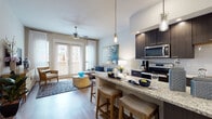 This single-story residence showcases a thoughtfully designed open-concept layout where the kitchen and living area flow seamlessly together. The kitchen is a standout feature, equipped with dark espresso cabinetry, granite countertops, stainless steel appliances, and a large peninsula island with seating for multiple guests. Glass pendant lights hang above the island, adding a refined touch. Light hardwood-style flooring runs throughout the main living spaces, contributing to a warm and cohesive aesthetic.

The living area is bright and inviting, benefiting from natural light provided by French doors that open to the exterior. A ceiling fan overhead enhances comfort, while the open sightlines to the kitchen make the space feel expansive and connected.

The bedroom is generously sized, featuring a ceiling fan, a large window dressed with sheer curtains, and warm hardwood-style flooring. A spacious walk-in closet with wire shelving provides ample storage. The bathroom continues the upscale finishes seen throughout, featuring granite countertops, an undermount sink with brushed nickel fixtures, and a tiled shower with a built-in niche. Overall, the residence presents a polished, contemporary ambiance with consistent, high-quality finishes.