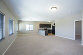 This single-floor unit presents a thoughtfully designed open-concept layout that seamlessly connects the kitchen and living areas. The kitchen is a standout feature, showcasing dark espresso cabinetry, granite countertops, and a full suite of black appliances, including a range, microwave, and refrigerator. Light hardwood flooring grounds the kitchen space, while a peninsula with an integrated sink and additional counter seating serves as a natural divider between the kitchen and the expansive carpeted living area. The living space is generously sized, bathed in natural light through multiple windows fitted with horizontal blinds, and illuminated by flush-mount ceiling fixtures. A ceiling fan adds comfort to one of the private rooms, which also benefits from its own window. The bathroom features a dark-cabineted vanity topped with granite, an undermount sink, chrome fixtures, and tile flooring, offering a clean and functional design. A dedicated laundry area houses a full-size washer and dryer alongside built-in shelving for added storage. Neutral taupe wall tones, white trim, and panel-style doors carry a consistent aesthetic throughout, giving the space a cohesive and move-in-ready feel.