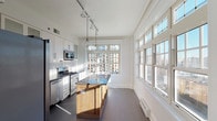 This single-floor residence combines classic architectural details with modern finishes throughout its thoughtfully designed layout. The living areas feature warm, polished hardwood floors and generous windows that invite abundant natural light and offer views of the surrounding cityscape. A fireplace anchors one of the main living spaces, adding a traditional focal point to the otherwise clean, contemporary aesthetic.

The kitchen is a standout feature, equipped with stainless steel appliances including a gas range, built-in microwave, and side-by-side refrigerator. White shaker cabinetry with glass-front uppers, a marble slab backsplash, dark countertops, and a central island with a wood base create a refined, functional workspace. Track and globe pendant lighting illuminate the room, which is further enhanced by an expansive bank of windows along one wall.

The bedrooms offer a calm retreat, with one featuring plush carpeting, crown molding, and access to an en-suite bathroom. A second bedroom includes hardwood floors, a large closet with paneled doors, and a French door entry. The bathrooms are well-appointed, one showcasing a glass-enclosed walk-in shower with white tile, and another featuring a soaking tub with distinctive penny-tile surround detailing.