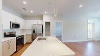 Located at 5000 Green Landing Dr in Cary, NC, this well-appointed 2-bedroom, 2-bathroom single-floor residence offers a clean, modern aesthetic throughout. The open-concept layout seamlessly connects the kitchen, dining, and living areas, creating an inviting and functional shared space. The kitchen is a standout feature, boasting a large white quartz island with an undermount sink, white upper cabinetry, warm wood-toned lower cabinets, a classic subway tile backsplash, and a full suite of stainless steel appliances including a refrigerator with ice maker, range, over-the-range microwave, and pendant lighting overhead. Warm hardwood-style flooring flows consistently throughout the entire residence, complementing the bright, neutral color palette. Both bedrooms are generously proportioned, with large windows that invite natural light and offer pleasant outdoor views of the surrounding greenery. The primary bedroom includes a ceiling fan and multiple windows. The two bathrooms are thoughtfully designed — one features a glass-enclosed walk-in shower with white subway tile, while the other offers a light wood vanity with a white countertop. Additional highlights include five closets providing ample storage, a dedicated laundry room with a full-size GE washer and dryer, and a hallway that connects the living spaces efficiently.