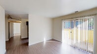 This single-floor residence offers a clean and functional layout designed for comfortable everyday living. The main living area is bright and open, featuring smooth hardwood-style flooring and neutral cream-toned walls that create a welcoming atmosphere. A sliding glass door with vertical blinds fills the space with natural light while providing access to an outdoor area, offering views of the surrounding exterior. The open flow of the layout connects the living area seamlessly to adjacent spaces.

The kitchen is thoughtfully designed with dark espresso cabinetry, granite-style countertops, and a full suite of stainless steel appliances including a refrigerator, stove, microwave, and dishwasher. A window with vertical blinds brings in additional natural light, making the kitchen feel bright and functional.

The bedroom is a comfortable, well-sized room with plush carpeting underfoot, neutral walls, and a window dressed with vertical blinds that allow for natural light and privacy. The bathroom is equipped with a full tub and shower combination featuring a curved curtain rod, a granite-topped vanity with dark cabinetry, and hardwood-style flooring, offering a polished and practical finish throughout.