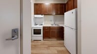 Located at Memphis Towers in Memphis, Tennessee, this one-bedroom, one-bathroom residence offers a practical and well-organized single-floor layout. The kitchen is a functional highlight, featuring rich dark-stained wood cabinetry that extends to the ceiling, providing ample storage. A coil electric range, an under-cabinet exhaust hood, a single-basin sink, and a full-size refrigerator complete the space, all set atop light-toned wood-style flooring that adds warmth to the room. The bedroom is carpeted for comfort and includes a built-in open closet with a hanging rod, offering convenient storage. A wall-mounted ventilation unit and a thermostat are also present, contributing to climate control. A sliding-door closet area is accessible nearby, adding additional storage flexibility. The bathroom is clean and straightforward, featuring a full-size soaking tub with a tiled shower surround equipped with built-in shelving, a wall-mounted pedestal sink with chrome fixtures, and wood-style flooring. Neutral tones throughout the unit — from the beige walls to the tan carpeting — create a calm, cohesive ambiance. Textured ceilings are consistent across the living spaces, lending a classic residential character to this efficiently designed Memphis Towers unit.