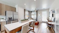 This thoughtfully designed single-floor residence offers a seamless blend of modern style and everyday functionality. The open-concept layout connects the kitchen, dining, and living areas into one cohesive, light-filled space. The kitchen is equipped with stainless steel appliances—including a refrigerator, range, built-in microwave, and dishwasher—complemented by light wood cabinetry, white quartz countertops, and wood-look flooring that flows throughout the home. A central island with a matching quartz surface provides additional prep and dining space, with seating for casual meals. The adjoining living area is bright and welcoming, featuring a ceiling fan, large windows with blinds and drape accents, and direct access to the outdoors through a full-lite glass door. The primary bedroom offers a comfortable retreat with natural light from a large window, a ceiling fan, and ample floor space. A secondary bedroom provides additional flexibility and similarly benefits from natural light. The bathroom is finished with warm wood-toned cabinetry, a white quartz vanity countertop, an undermount sink, a glass-enclosed shower and tub combination, and a hexagonal wall-mounted shelf for decorative storage. Recessed lighting, neutral wall tones, and consistent wood-look flooring throughout tie the entire space together with a clean, contemporary aesthetic.
