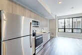 Located at 960 Greene St in Ann Arbor, Michigan, this modern studio offers a thoughtfully designed open-concept layout that efficiently combines the kitchen, dining, and living areas into a single bright, cohesive space. Light-toned wood-style flooring runs throughout, lending warmth and visual continuity, while neutral walls and recessed lighting create a clean, contemporary aesthetic.

The kitchen is a standout feature, outfitted with a full suite of stainless steel appliances — including a refrigerator, electric range, built-in microwave, and dishwasher — paired with light wood cabinetry extending to the ceiling for ample storage. A white countertop and subway tile backsplash complete the polished look. Large windows flood the living area with natural light and provide views of the surrounding neighborhood.

The bathroom is finished with modern fixtures, featuring a glass-enclosed walk-in shower with a built-in bench, a wood-toned vanity, and a white quartz countertop. Two closets offer generous storage, and an in-unit laundry area adds everyday convenience. The overall design is clean, functional, and well-suited for comfortable urban living in Ann Arbor.
